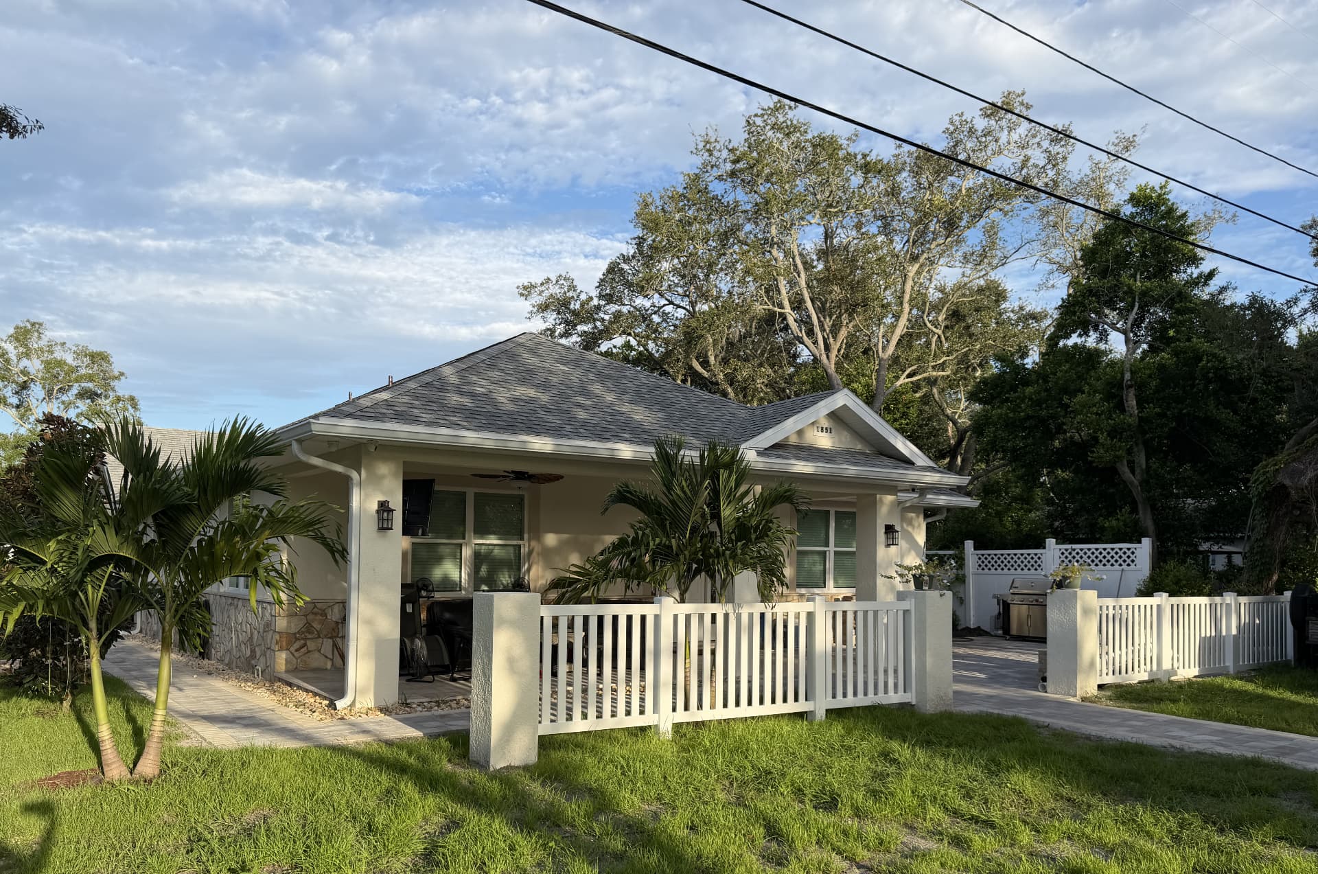 Completed Tarpon Springs custom home with a covered porch, palm landscaping, white fence, and finished driveway