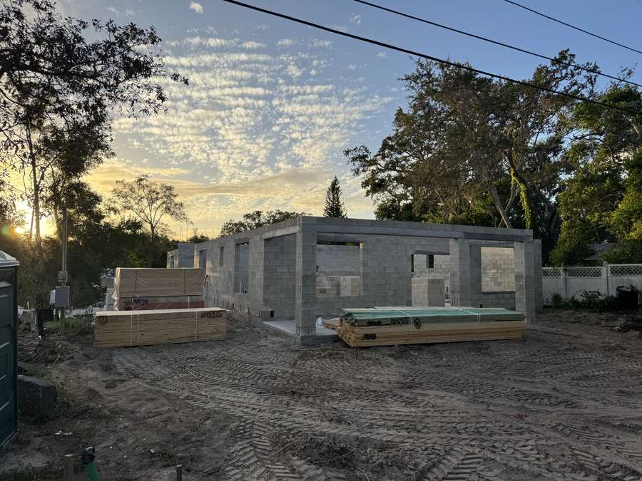 Completed concrete block walls with window openings and roof framing lumber staged at the job site